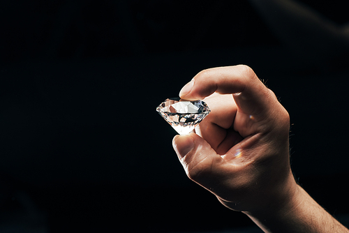 partial view of man holding big clear shiny diamond isolated on black