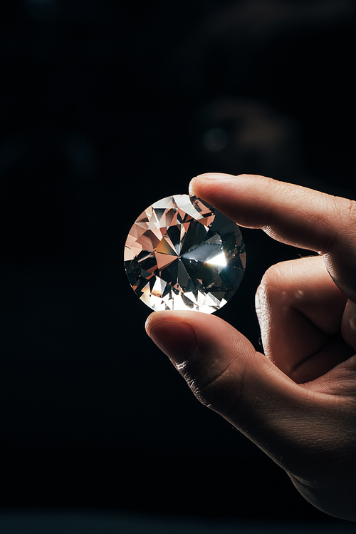 cropped view of man holding big clear shiny diamond on black background