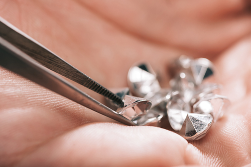 close up of tweezers near shiny diamonds in hand
