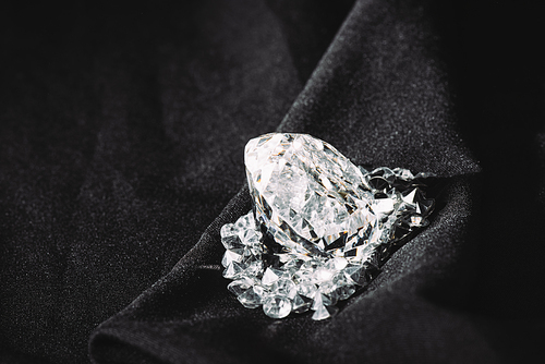 sparkling big diamond among small on black textured shiny cloth
