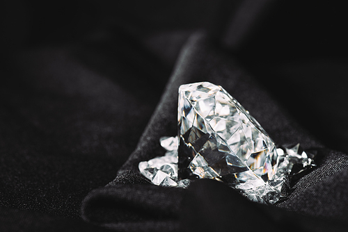 sparkling pure big diamond among small on black textured shiny cloth