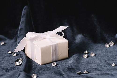 gift box with white ribbon and bow near pure diamonds on blue cloth