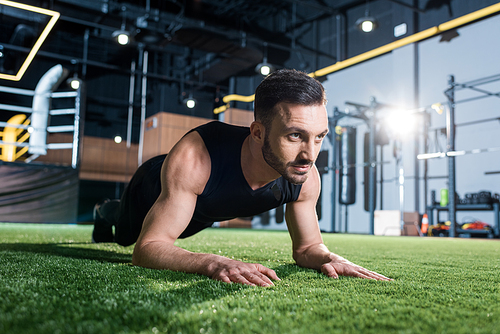 handsome bearded man doing plank exercise on green grass