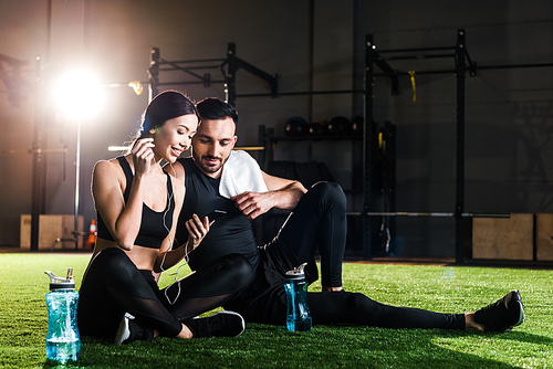 handsome man sitting on grass and looking at smartphone in hands of beautiful woman