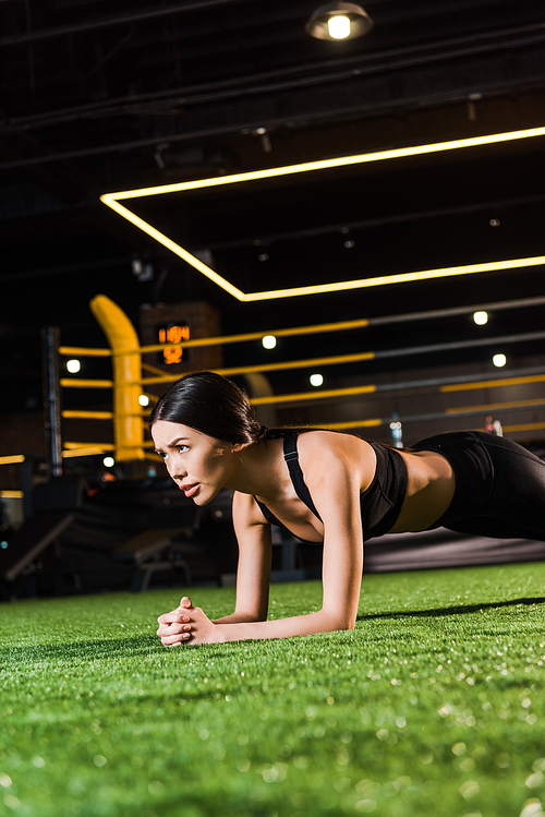 selective focus of attractive woman doing plank exercise on grass