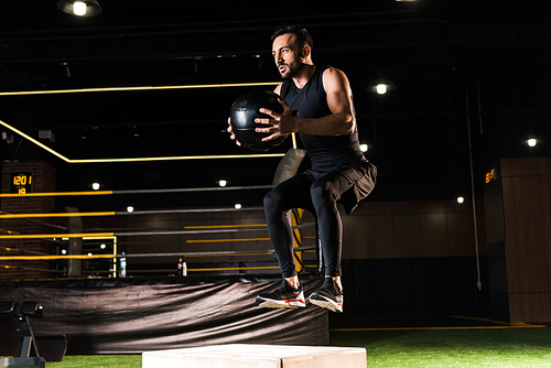 low angle view of serious man jumping on  box while holding ball