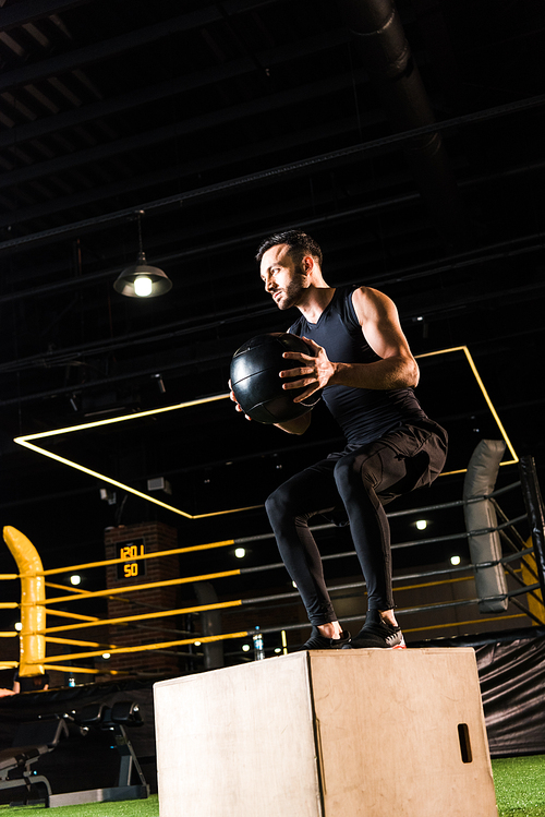 low angle view of serious man doing on squat box while holding ball