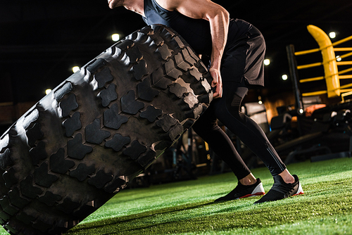 cropped view of strong man working out with huge car tire on green grass