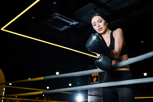 low angle view of upset woman looking at boxing gloves while standing in gym