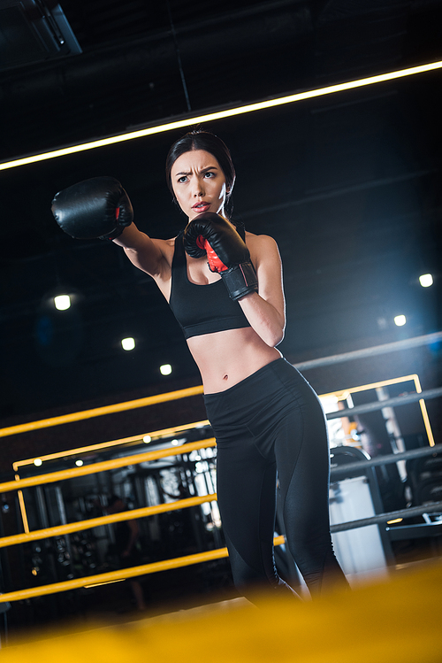 selective focus of young woman boxing while standing in boxing gloves in gym