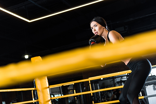 selective focus of athletic woman boxing while standing in boxing gloves in gym