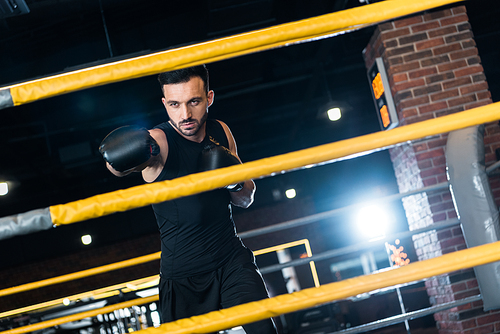 selective focus of strong man in boxing gloves working out in gym
