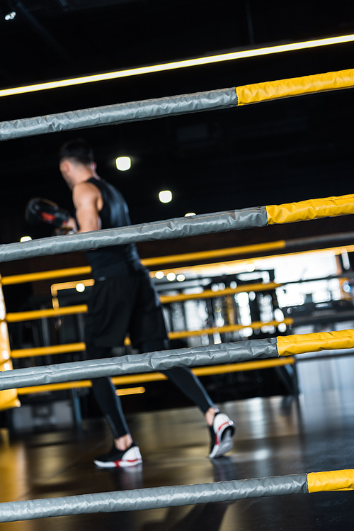 selective focus of boxing ring surrounded by ropes near man exercising in boxing gloves