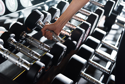 cropped view of athletic young woman taking heavy dumbbell in gym