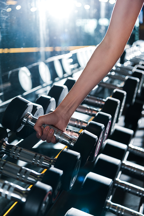 cropped view of sportswoman taking dumbbell in gym