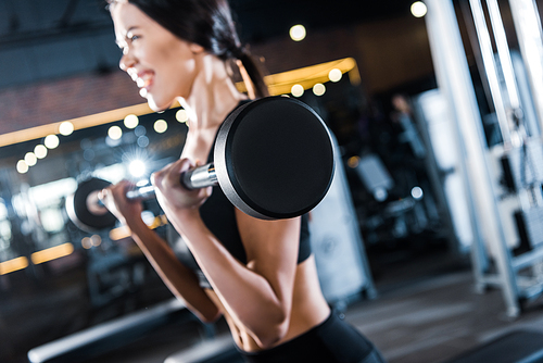 selective focus of young woman working out with heavy barbell in gym