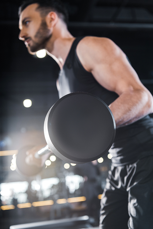 selective focus of handsome strong man exercising with heavy barbell in gym