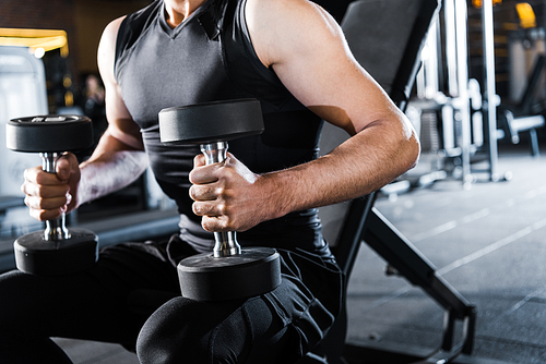 cropped view of athletic man working out with dumbbells in gym