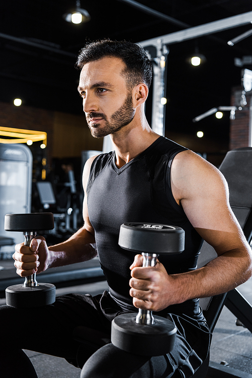 handsome athletic man working out with dumbbells in gym