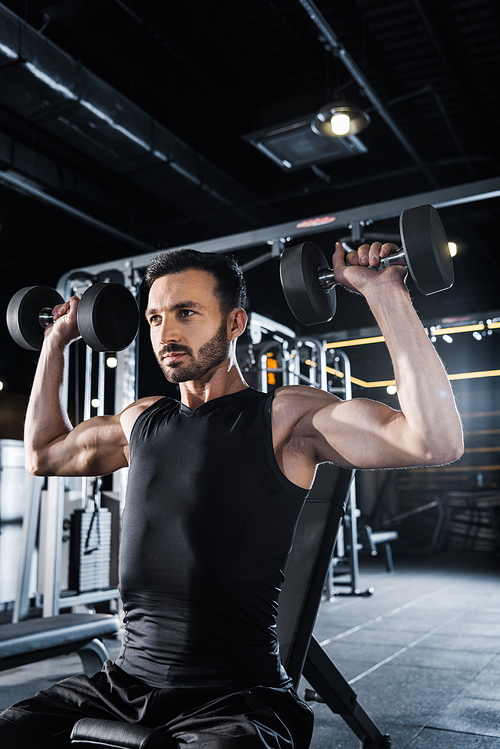 low angle view of strong man working out with dumbbells in gym