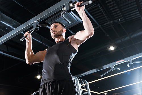 low angle view of handsome sportsman doing pull up in sports center