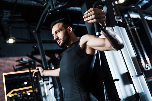 low angle view of strong sportsman in sportswear exercising on training apparatus in gym