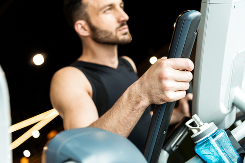 selective focus of sport bottle near handsome athletic man working out on exercise bike