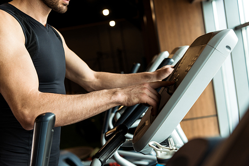cropped view of man in sportswear pointing with finger at exercise bike in gym