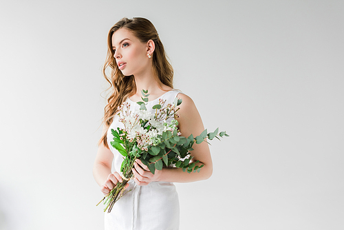 pensive young woman in dress holding flowers on grey