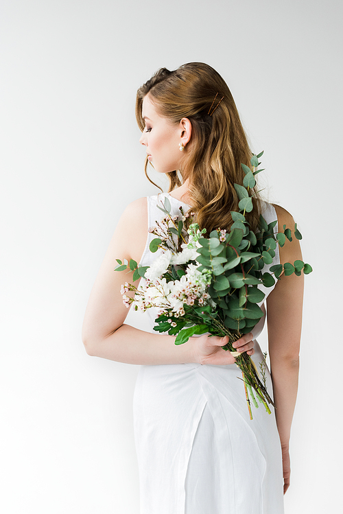 back view of woman in elegant dress holding flowers behind back on white