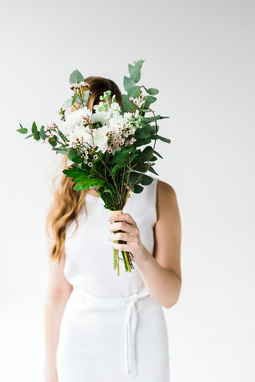 girl in dress covering face with flowers on white