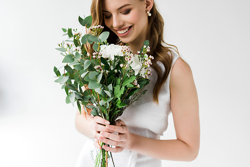 cheerful young woman looking at flowers and smiling on white