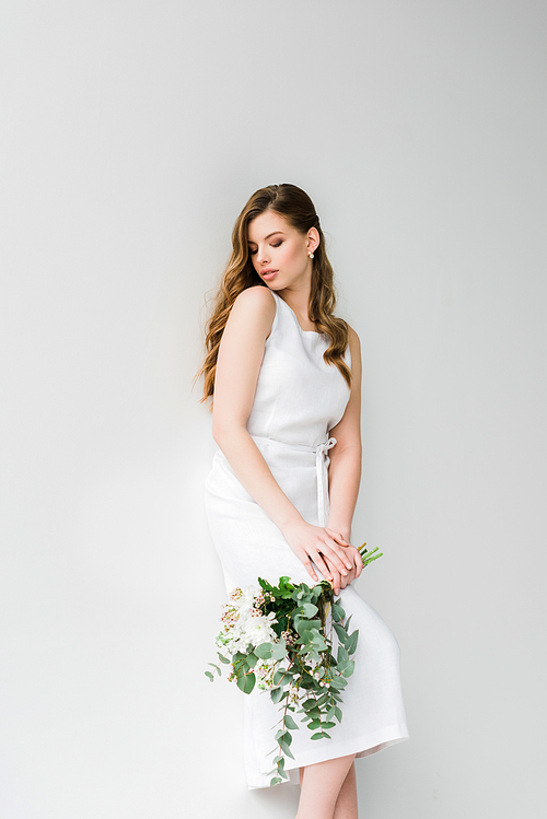 woman in dress holding bouquet of flowers with eucalyptus leaves on white