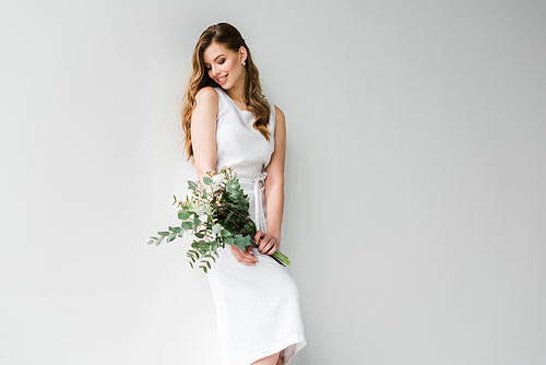 smiling woman in dress holding bouquet of flowers with eucalyptus leaves on white