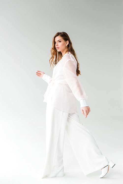 beautiful and stylish young woman walking on white