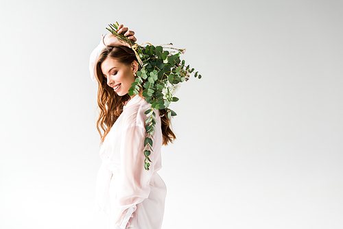 cheerful beautiful girl holding flowers with green eucalyptus leaves behind back on white