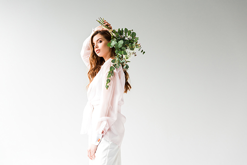 beautiful young woman holding flowers with green eucalyptus leaves behind back on white