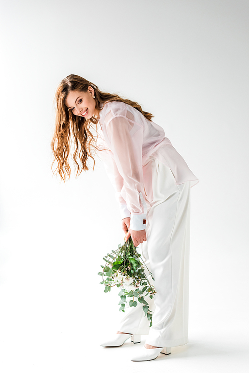 happy and stylish young woman holding flowers with eucalyptus leaves on white
