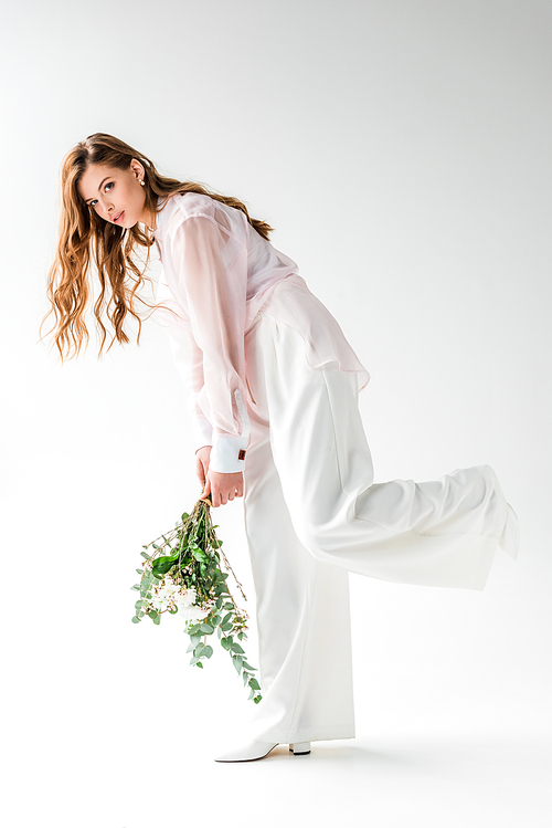 stylish young woman holding flowers with eucalyptus leaves on white