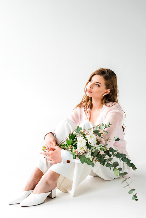 young woman sitting with bouquet of flowers and green eucalyptus leaves on white