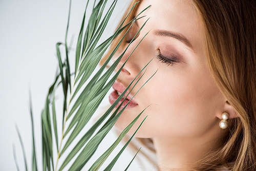 attractive girl with closed eyes near green palm leaf on white