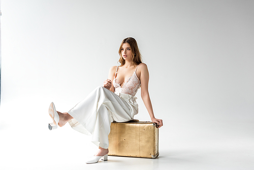 attractive young woman sitting on travel bag on white