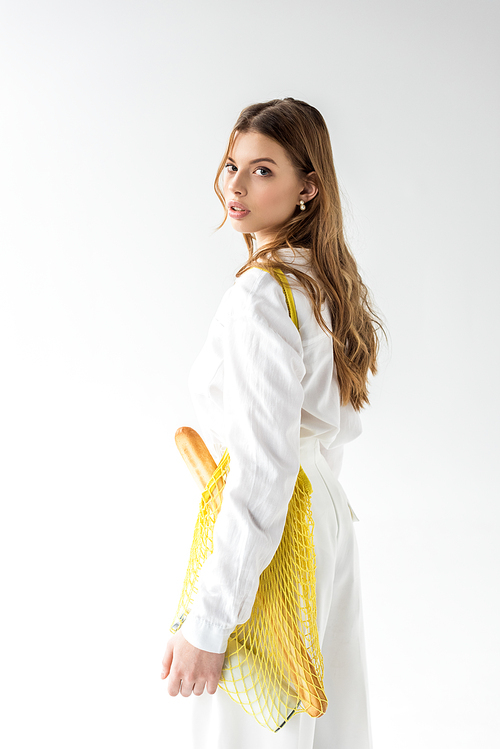 attractive woman with baguette and bottle of milk in yellow string bag on white