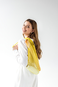 happy young woman holding yellow string bag with baguette and bottle of milk on white