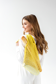 smiling young woman holding yellow string bag with baguette and bottle of milk on white