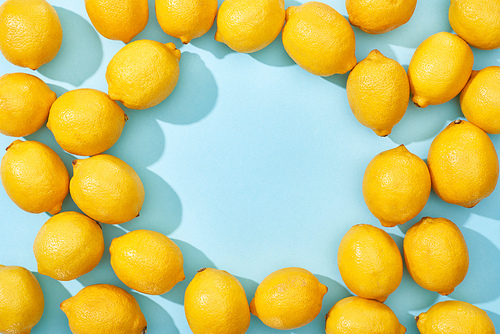 top view of ripe yellow lemons on blue background with shadows and copy space