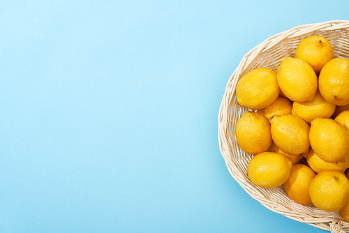 top view of ripe yellow lemons in wicker basket on blue background with copy space
