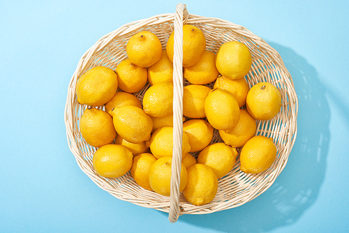 top view of ripe yellow lemons in wicker basket on blue background