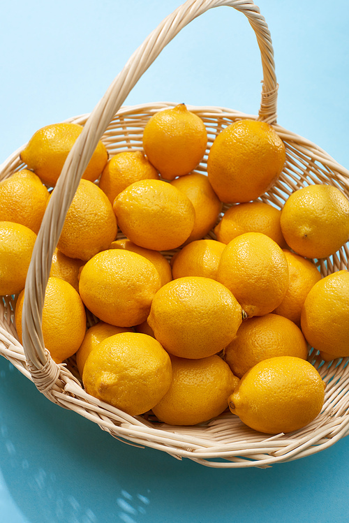 ripe yellow lemons in wicker basket on blue background