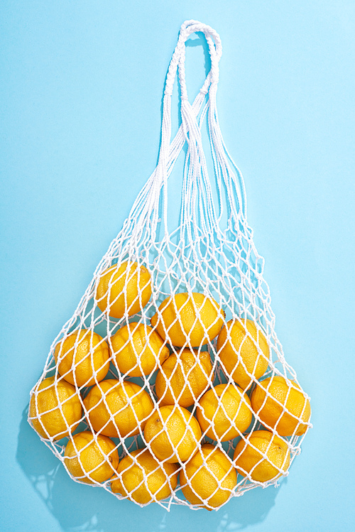 top view of ripe yellow lemons in string bag on blue background